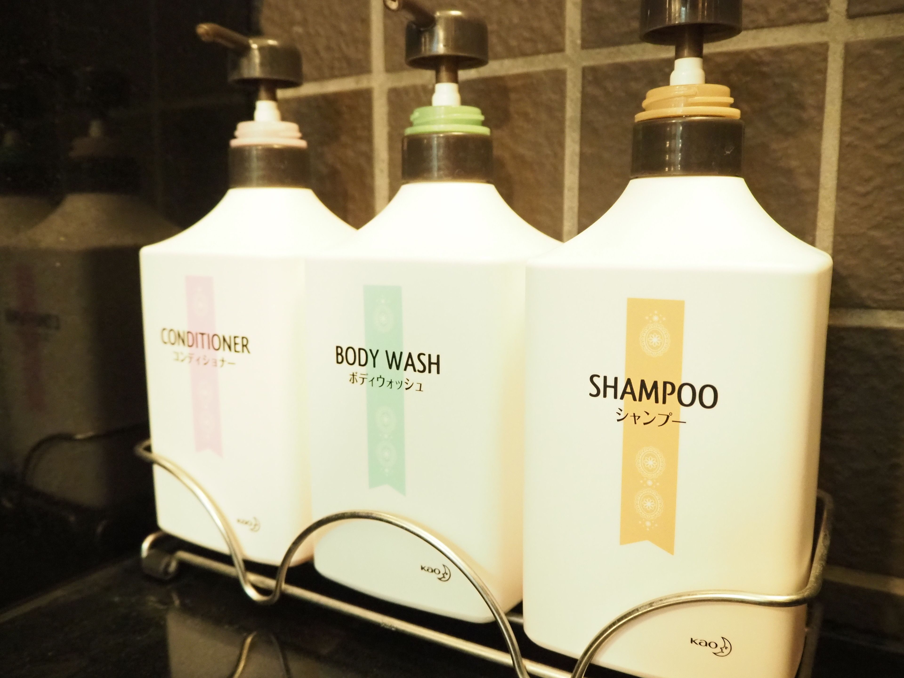 Drei Flaschen Shampoo, Conditioner und Duschgel auf einem Metallgestell.