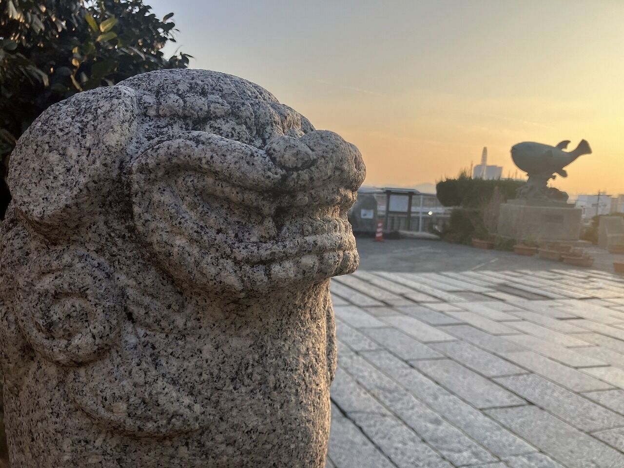 A stone lion statue in a courtyard with a paved floor and a building in the background.