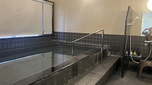 Een moderne spa-ruimte met een glazen hottub, een metalen reling en een klein zithoekje met een kruk.