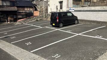 A parking lot with marked spaces, a black van parked, and buildings in the background.