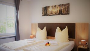 A double bed with white linens, two pillows, and a bedside table with a lamp. - Hotel Restaurant Tüxen (Rendsburg)