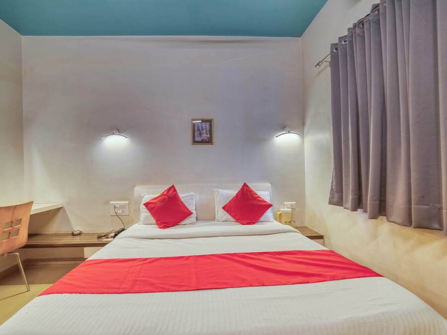 A hotel room with a bed, a desk, and a chair. There are two wall-mounted lights and a picture on the wall.