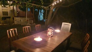 An outdoor wooden table with chairs, lit by lanterns, surrounded by greenery and string lights. - Amazing apartments 2025 (Willemstad)