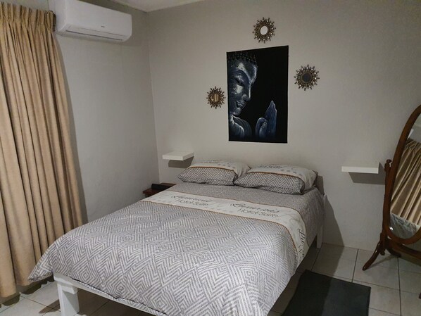 A bedroom with a bed, a nightstand, a wall-mounted air conditioner, a mirror, and decorative wall art. - Amazing apartments 2025 (Willemstad)