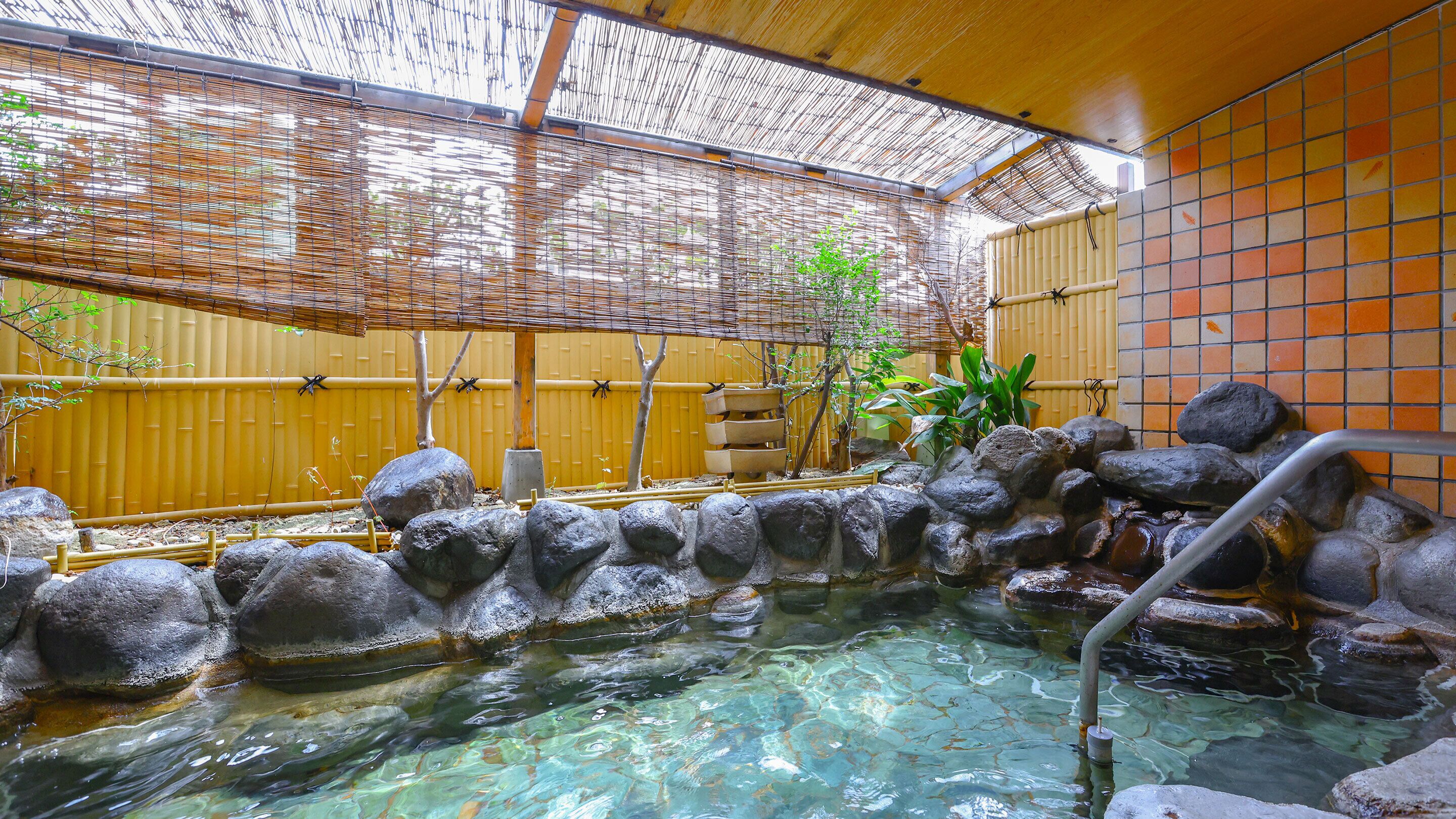 Un onsen japonés tradicional con agua cristalina, un baño de piedra y una valla de bambú.
