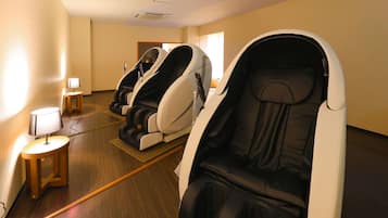 A room with massage chairs, a small table with a lamp, and wooden flooring.