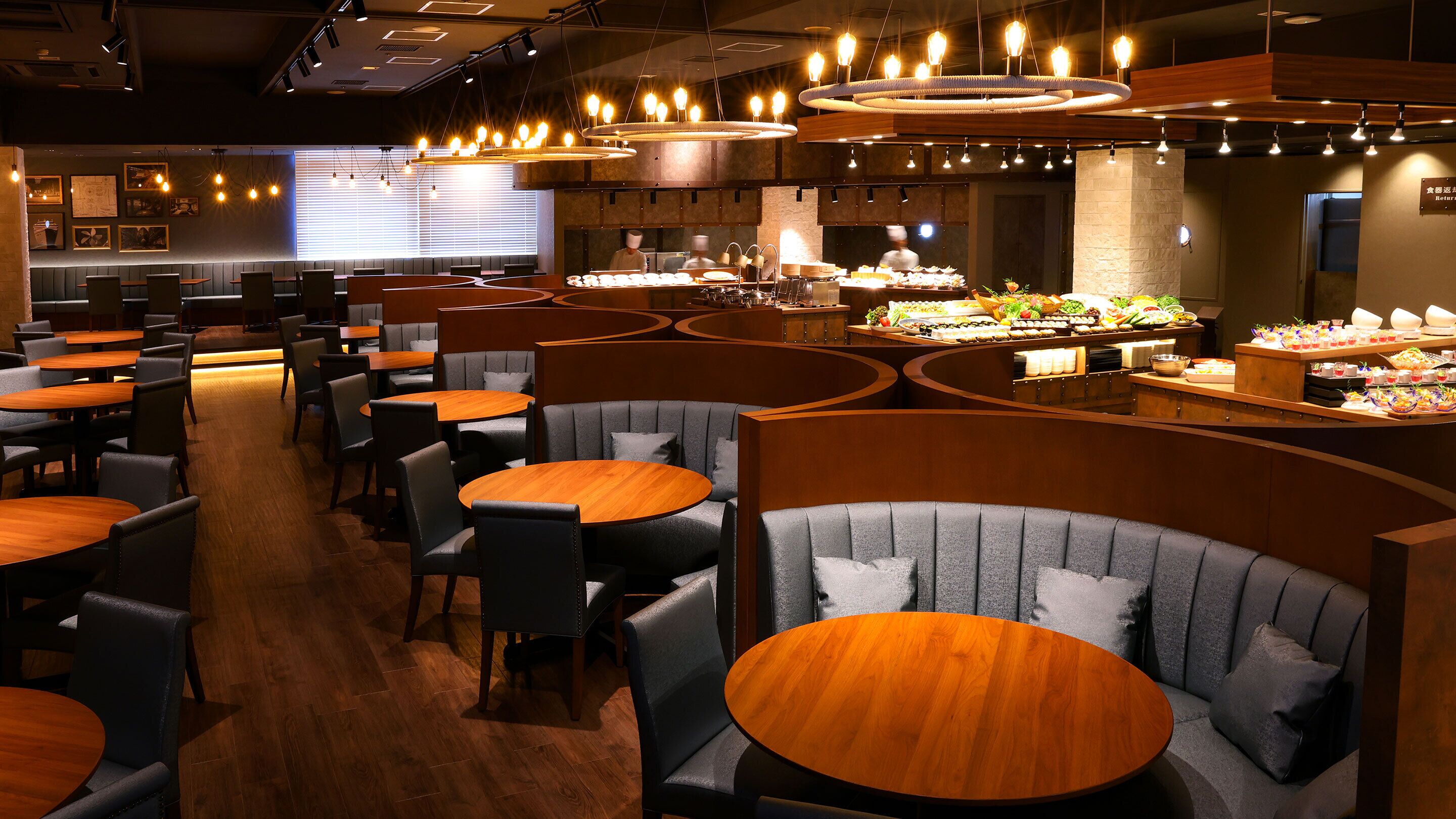 A restaurant with round tables and booths, a buffet area, and a chef in the background.