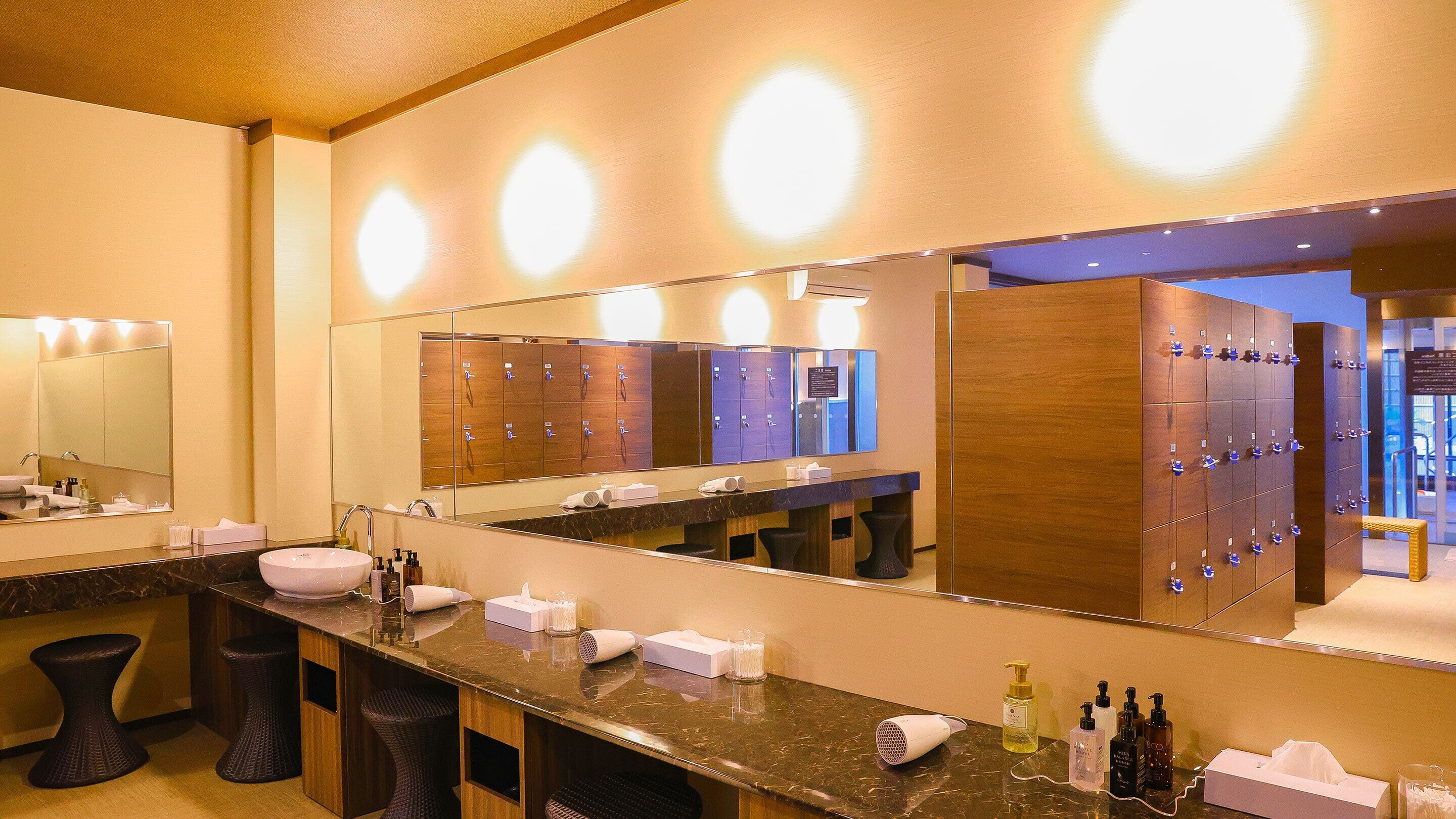 A modern bathroom with a large mirror, multiple sinks, and lockers.