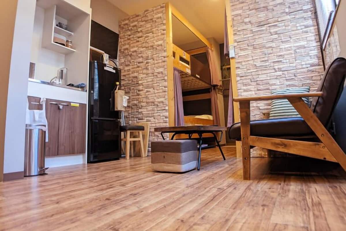 A modern living room with a sofa, a dining table, and a kitchen area with cabinets and a refrigerator.