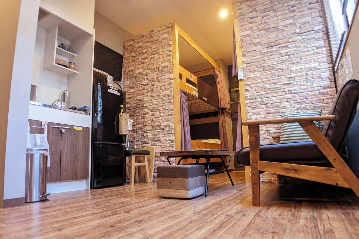 A modern living room with a wooden floor, a sofa, a dining table, and a kitchen area with a refrigerator and cabinets.