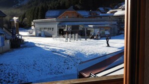 A snow-covered outdoor area with a building that appears to be a hotel or lodge, featuring a wooden facade and a signboard. - Base-Camp Appartement (Irdning-Donnersbachtal)
