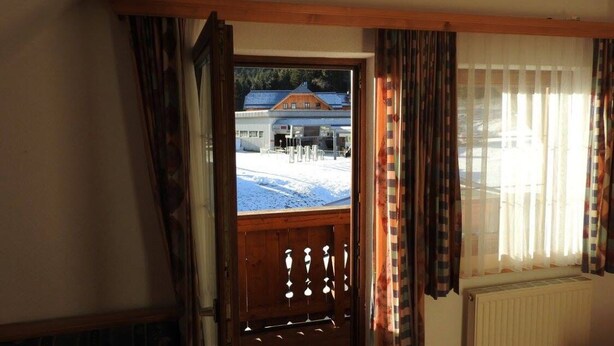 A room with a wooden door leading outside, a window with curtains, and a view of a snowy landscape. - Base-Camp Appartement (Irdning-Donnersbachtal)