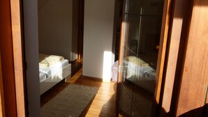 A narrow hallway with two beds, a wooden floor, and a large glass door. - Base-Camp Appartement (Irdning-Donnersbachtal)