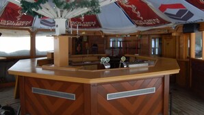 A bar area with a wooden counter and a ceiling decorated with banners and a Christmas tree. - Base-Camp Appartement (Irdning-Donnersbachtal)