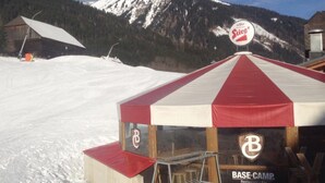 A BASE-CAMP restaurant/bar with a red and white striped tent, a mountain backdrop, and a sign indicating 'Stieg'. - Base-Camp Appartement (Irdning-Donnersbachtal)