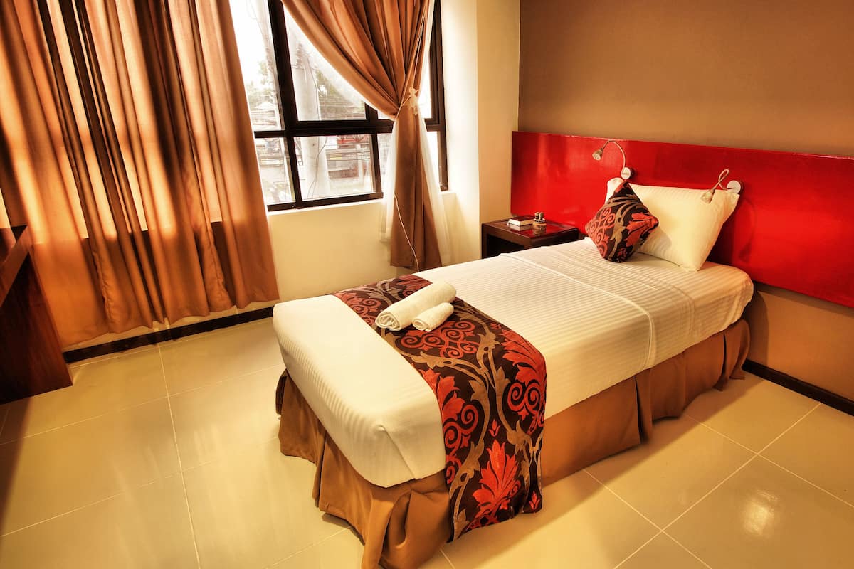 Quarto de hotel com cama, cortinas, mesa de cabeceira e uma parede em destaque na cor vermelha.