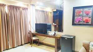 Ein Zimmer mit Schreibtisch, Stuhl, Fernseher und kleinem Kühlschrank.
