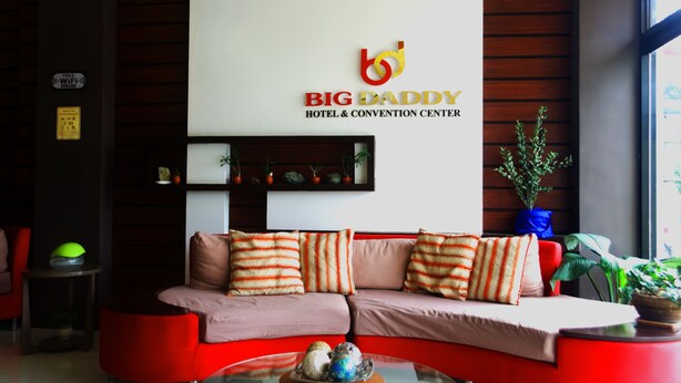 Ein Empfangsbereich mit einer roten Couch, einer weißen Wand mit dem Schild 'Big Daddy Hotel & Convention Center' und einem kleinen Regal mit Dekoration.