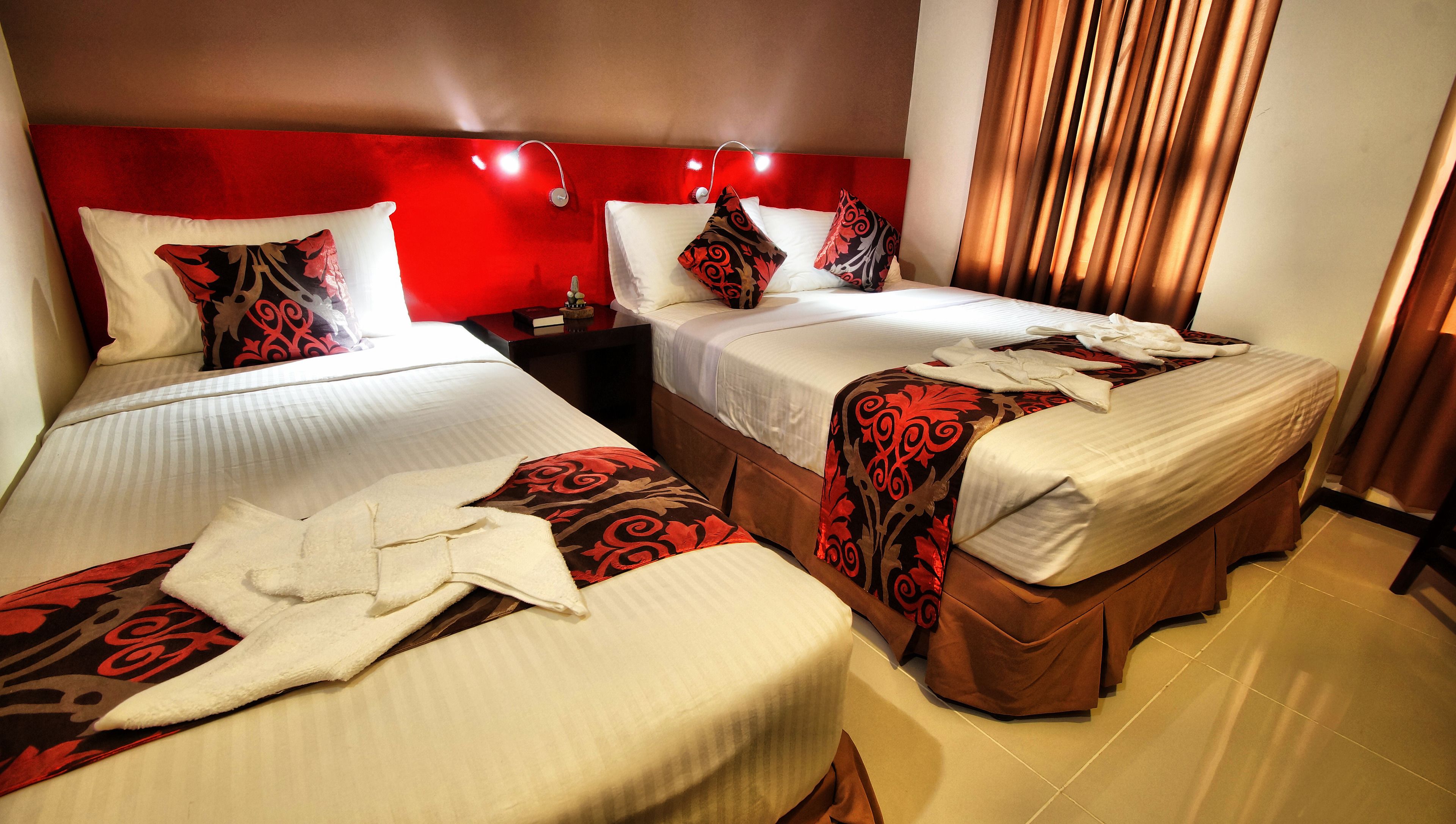 A hotel room with two beds, red headboard, and a nightstand with a lamp.