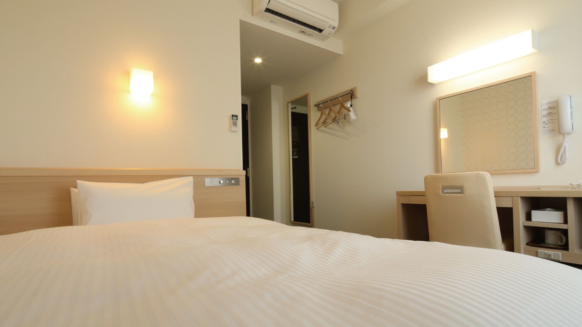 Een hotelkamer met een bed, nachtkastje, stoel, bureau, spiegel en telefoon.