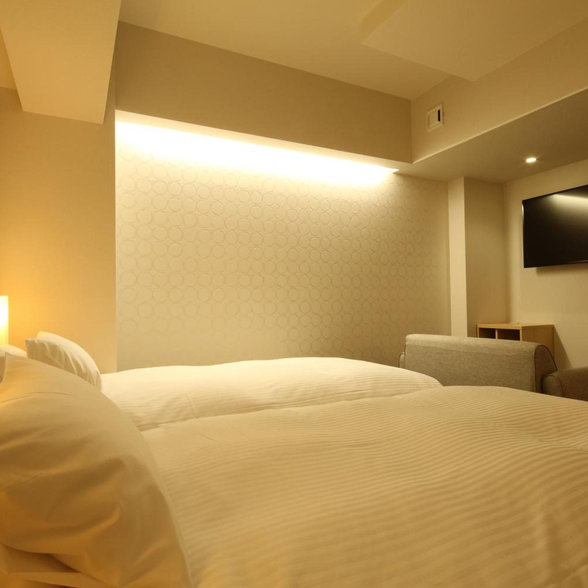 Una habitación de hotel con dos camas, un televisor de pantalla plana montado en la pared y un papel tapiz estampado.