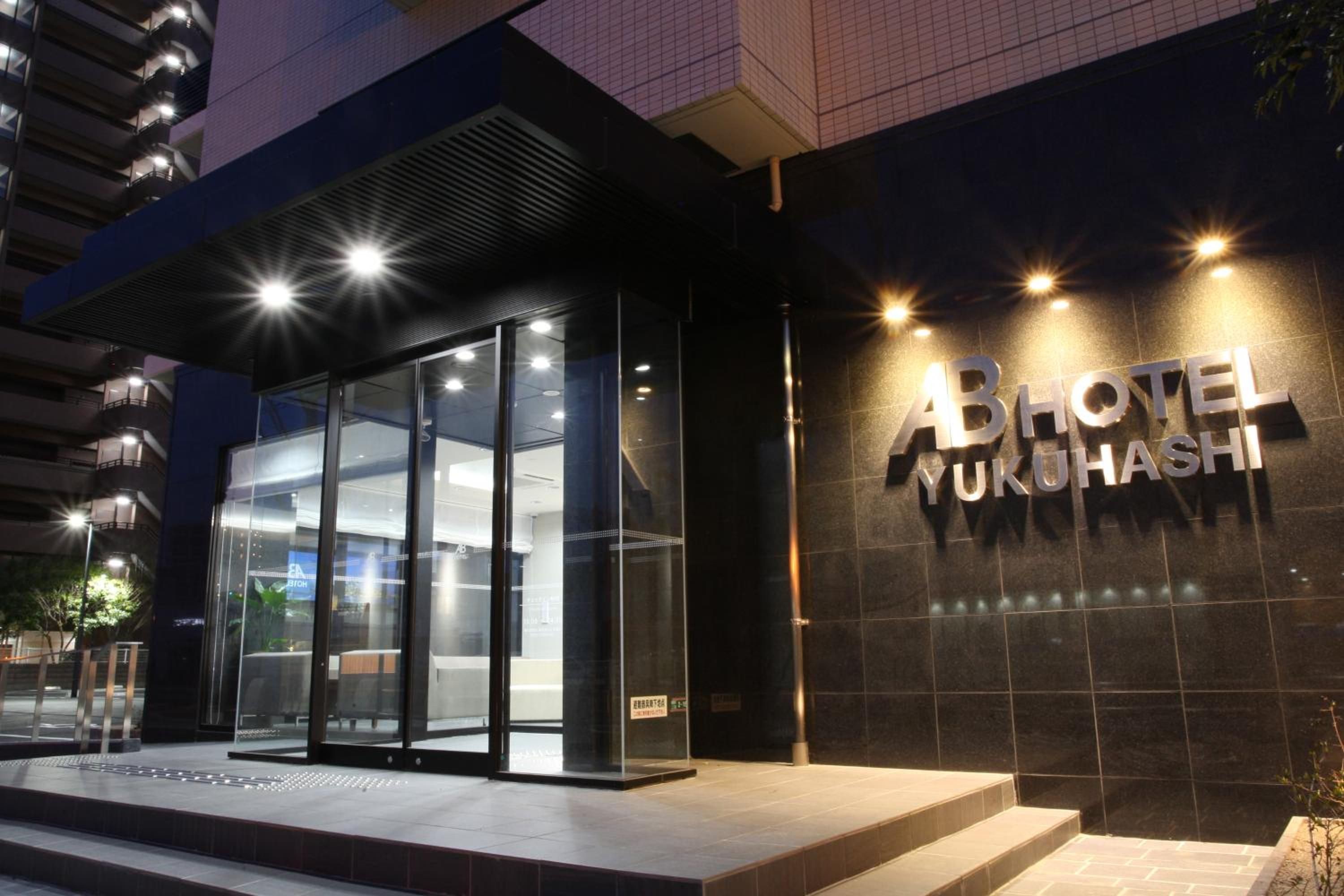 Una entrada de hotel moderna con fachada de vidrio y un cartel que dice 'ABHOTEL YUKUSHI'.