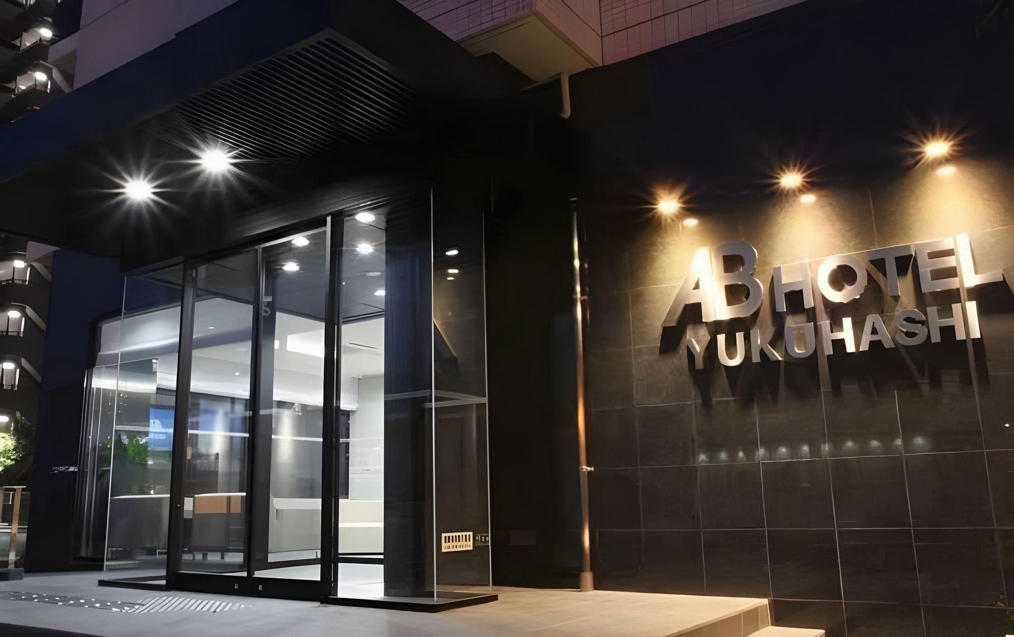 Exterior del HOTEL AB NUKUHASHI, con fachada de vidrio moderno y señalización iluminada.