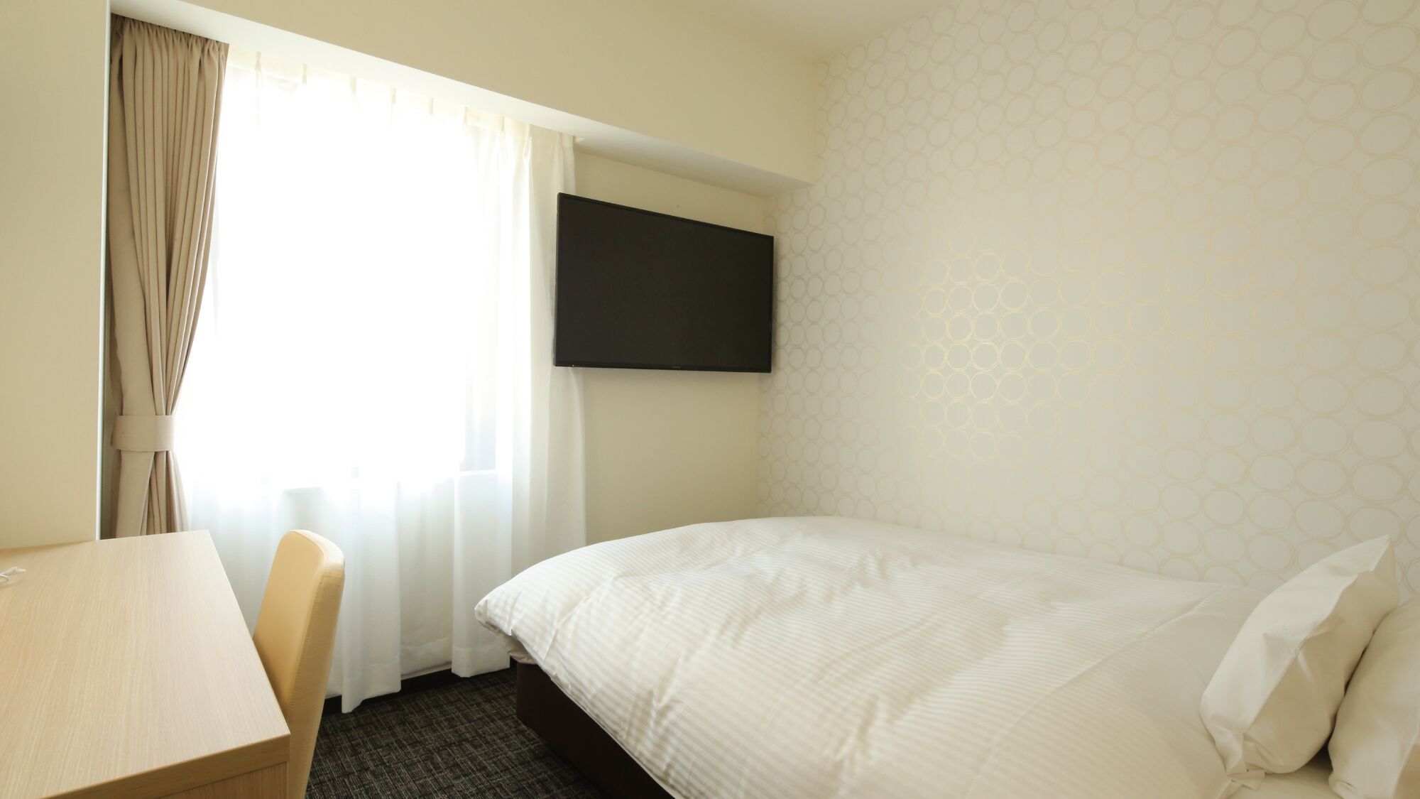 Een hotelkamer met een bed, een aan de muur bevestigde televisie, een bureau en een stoel.