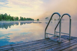 A wooden dock with metal railings extending into a calm lake, surrounded by trees and mist. - Puttererseehof (Aigen im Ennstal)