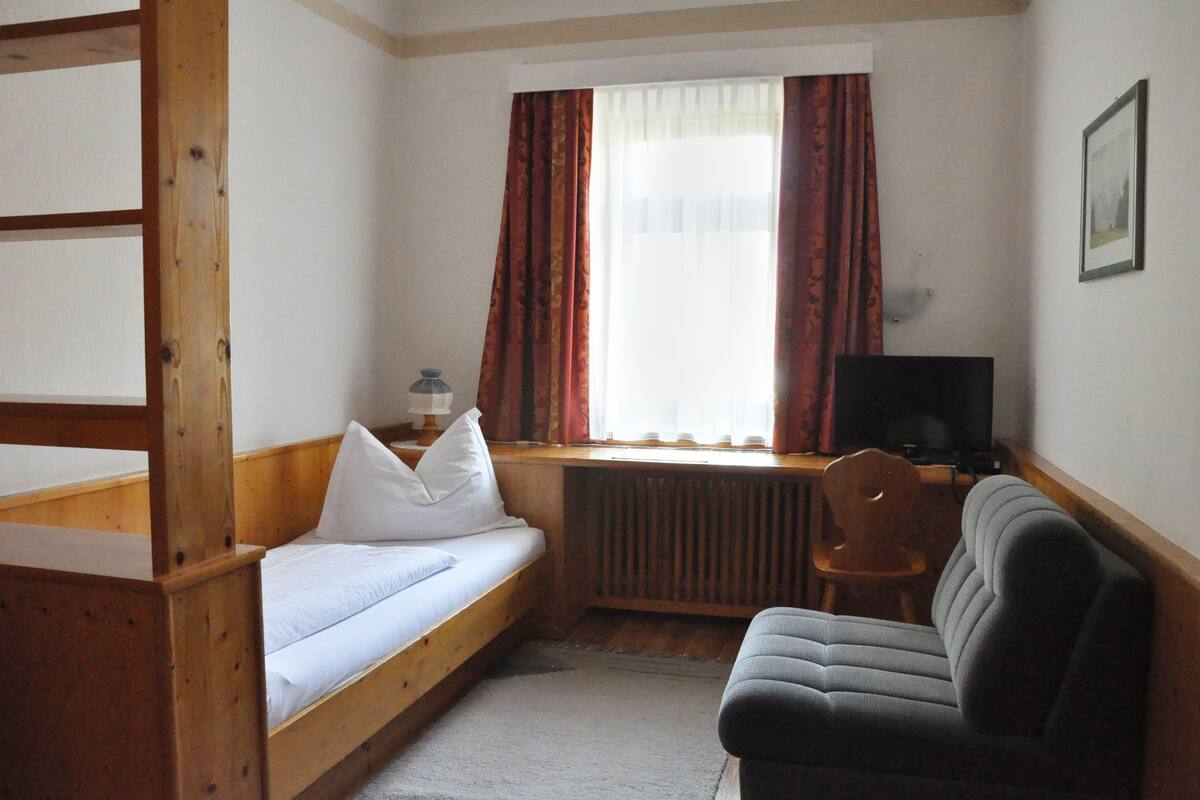 A room with a bunk bed, a desk with a chair, a sofa, a radiator, and a television.