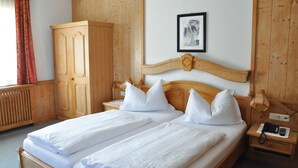 A double bed with white linens, a wooden wardrobe, a bedside table with a lamp, and a framed picture on the wall.