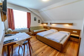 A room with a wooden bed, a desk with a chair, a window with curtains, and a radiator. - Puttererseehof (Aigen im Ennstal)