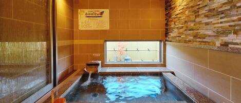 A hot spring bath with a stone wall, a window, and a sign.