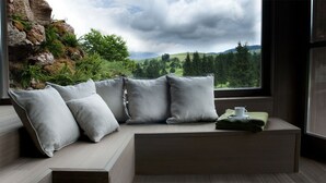 A modern room with a built-in bench seating area, a window with a view of a forest and hills, and a small table with a cup and a folded green towel. - Meltar Boutique Hotel (Asiago)