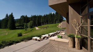 A modern building with a deck and outdoor seating area overlooking a forested hillside. - Meltar Boutique Hotel (Asiago)
