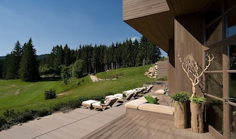 Un edificio moderno con terraza y zona de estar exterior con vistas a un paisaje boscoso.