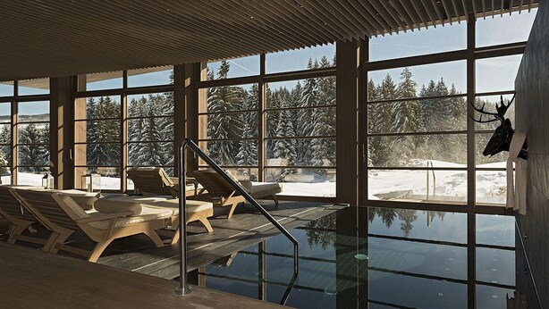 An indoor swimming pool with wooden loungers and a view of a snowy landscape through large windows. - Meltar Boutique Hotel (Asiago)