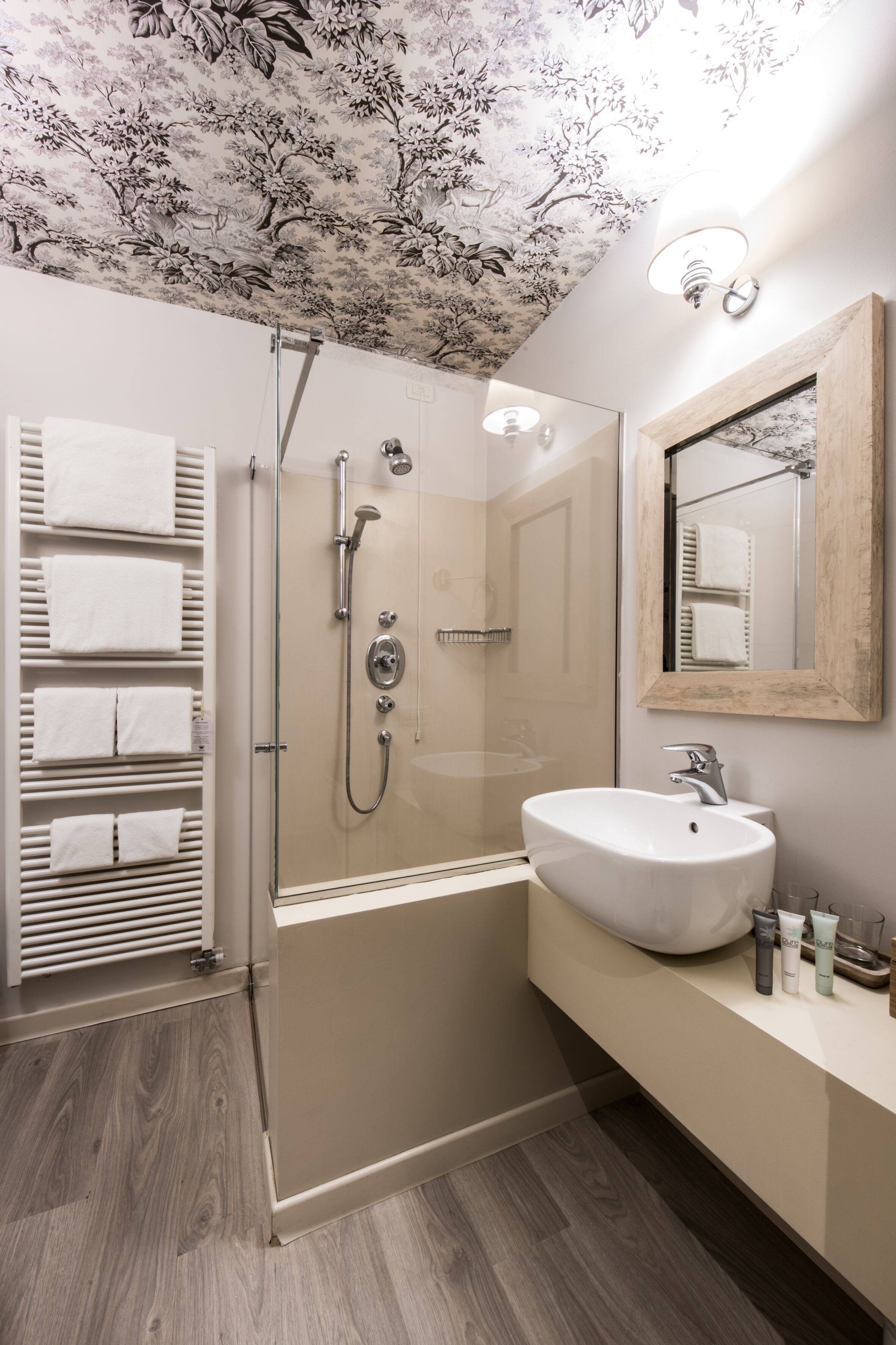 A modern bathroom with a glass-enclosed shower, a large white sink, and a wooden-framed mirror.
