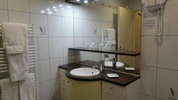 Ein Badezimmer mit Waschbecken, Spiegel, Handtuchhalter und einem an der Wand befestigten Föhn.