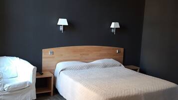 A bedroom with a wooden headboard, a bed with a quilt, a bedside table, a nightstand, and two wall-mounted lamps.