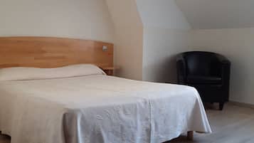 Un dormitorio con cama, una silla y techo inclinado.