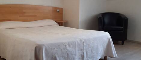 Un dormitorio con cama, una silla y techo inclinado.