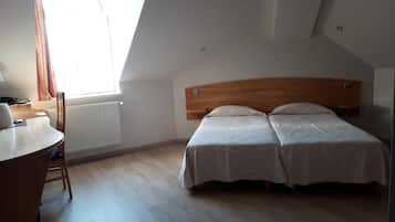 A bedroom with a wooden headboard, two beds, a desk, and a window with curtains.