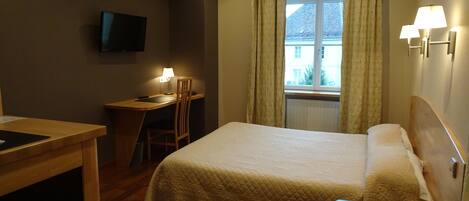 Habitación de hotel con cama, escritorio con silla, televisor en la pared y ventana con cortinas.