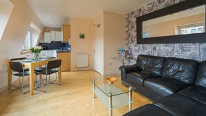 Ein modernes Wohnzimmer mit einem Glastisch, einer schwarzen Ledersofa und einem Essbereich mit einem Holztisch und Stühlen.