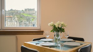 A dining table set with plates, cutlery, and a vase of flowers, with a view of a historic building through a window. - Rose Street Apartment City Centre (Edinburgh)