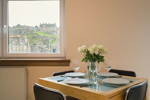 A dining table set with plates, cutlery, and a vase of flowers, with a view of a historic building through a window.