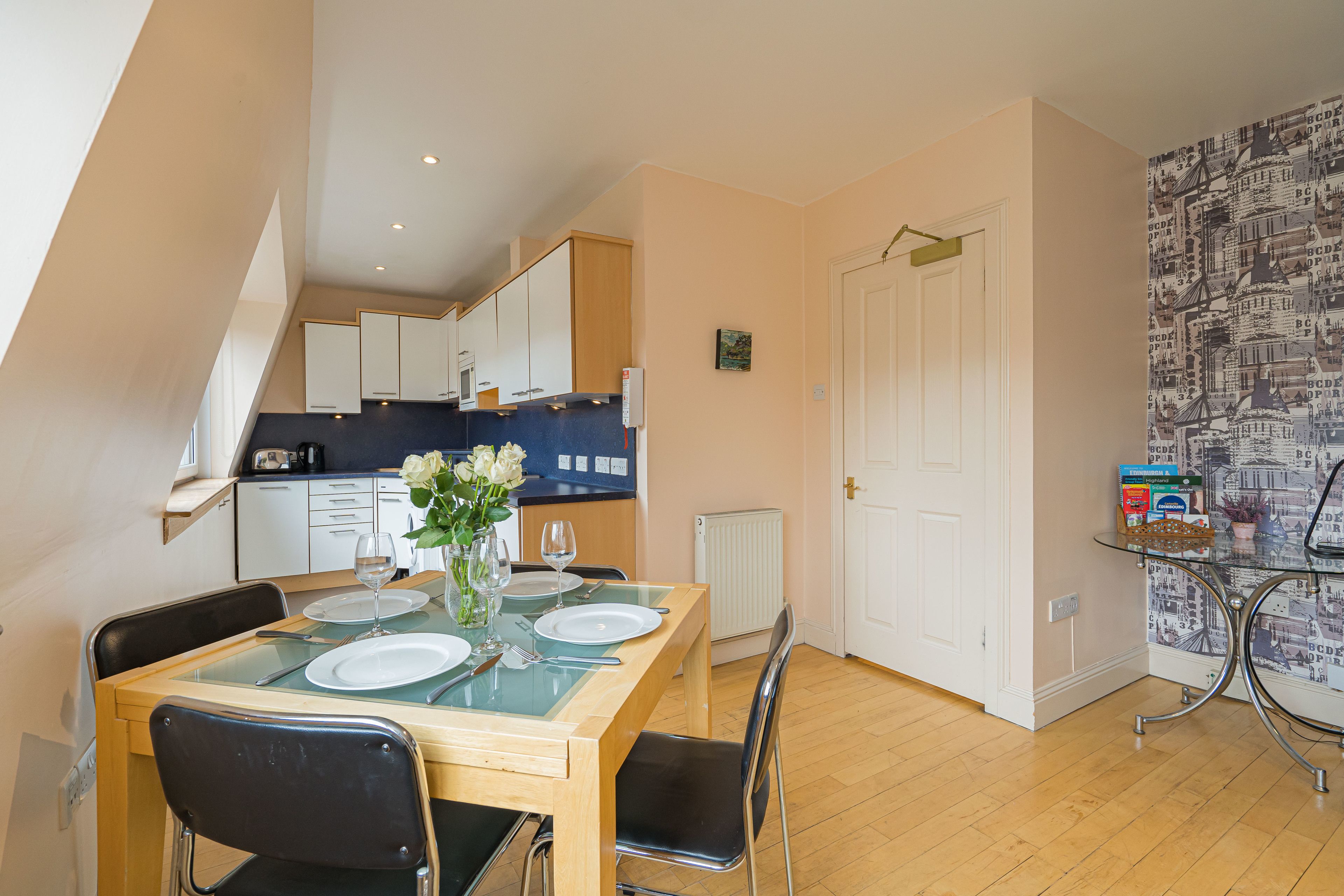A dining area with a table set for four, a kitchen in the background, and a cityscape wallpaper on the adjacent wall.