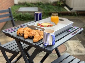 Aamiaispöydällä on croissantteja, muki, lasi appelsiinimehua ja kulho täynnä hedelmiä.