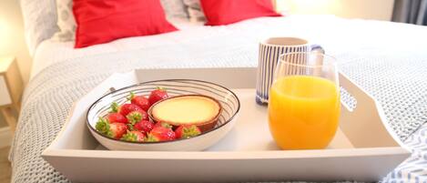 A breakfast tray with strawberries, a slice of cheesecake, and a glass of orange juice on a bed with red pillows.